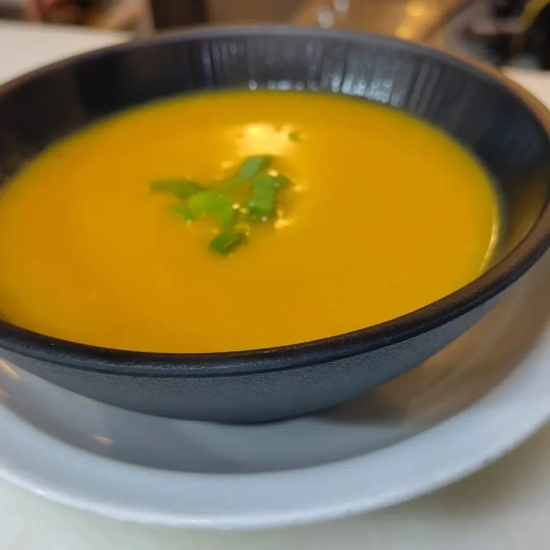 A dark bowl of smooth orange soup with a small herb leaf