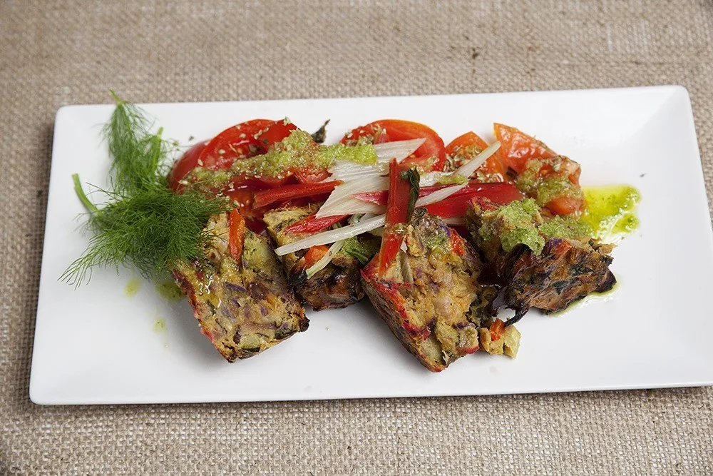 Slices of a chopped vegetable terrine with fresh fennel and sliced tomato on a rectangular white plate