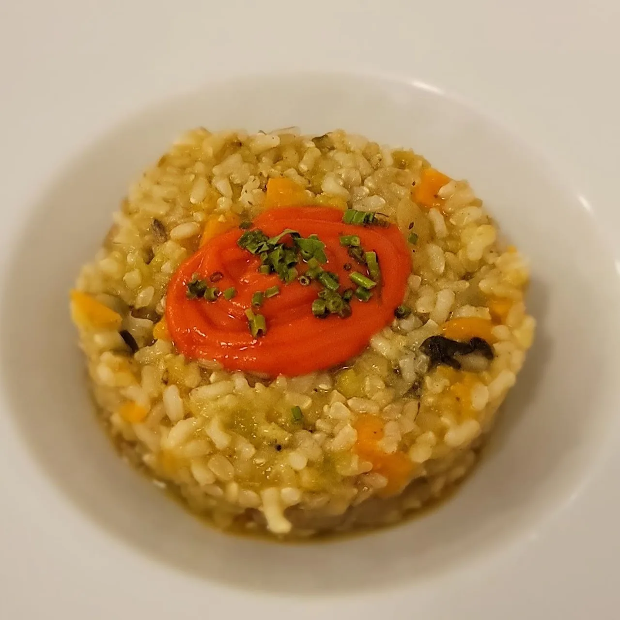 A round mound of rice with a red pepper sauce and herbs on a white plate