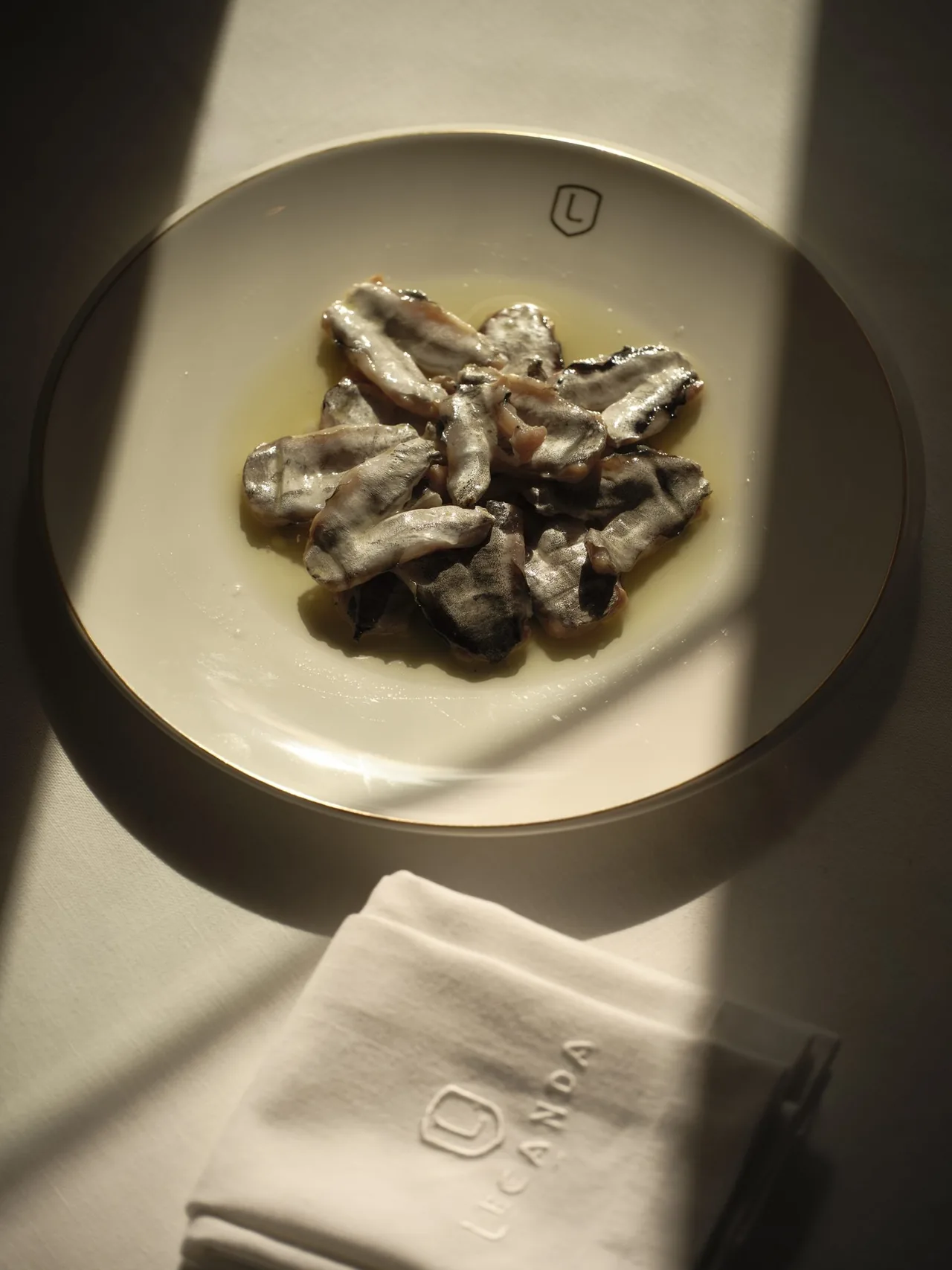 Small silvery anchovies on a cream plate beside a folded napkin
