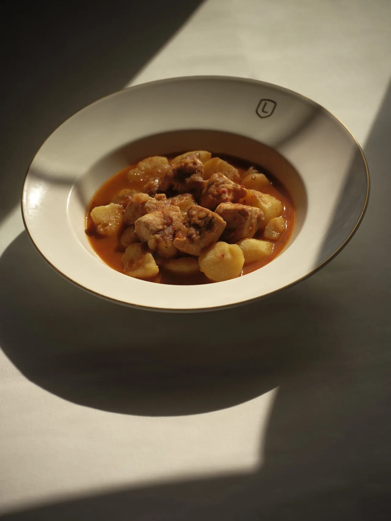 A white bowl of stew with chunks of potato and meat