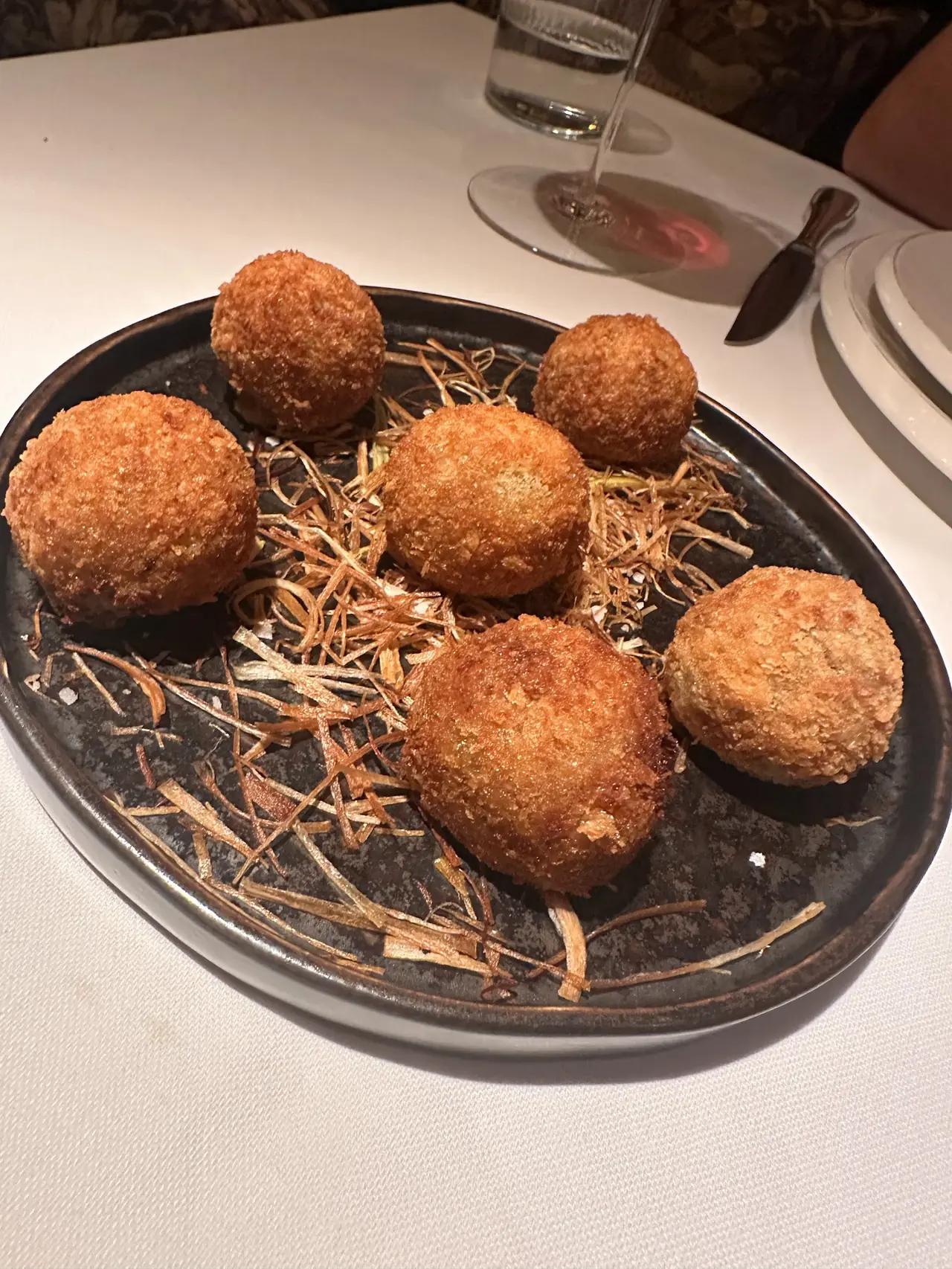Six golden fried breaded croquettes served on a bed of crispy fried leek strands on a dark oval plate