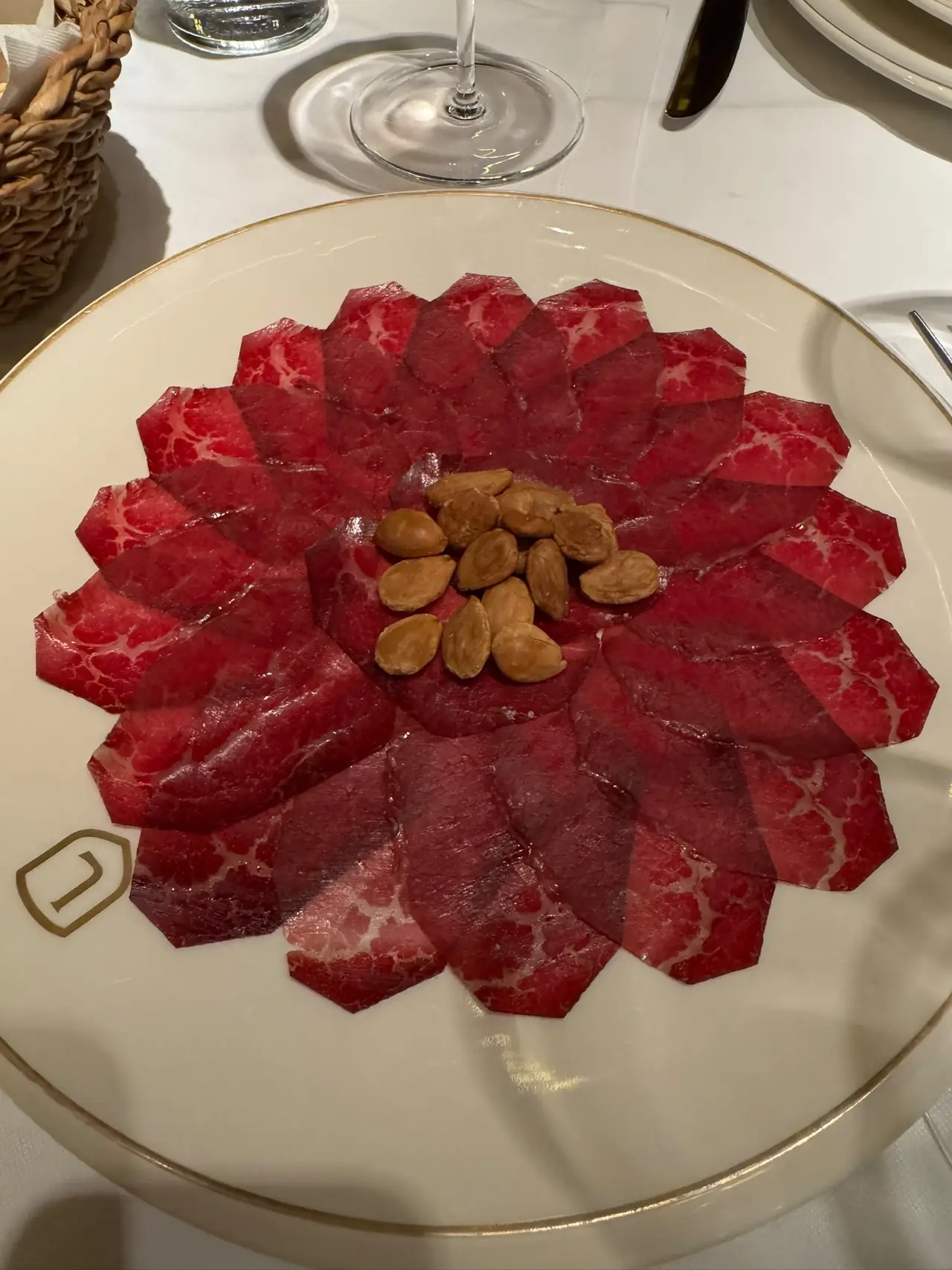 Thin slices of cured beef arranged in a flower pattern around a pile of whole almonds on a white plate
