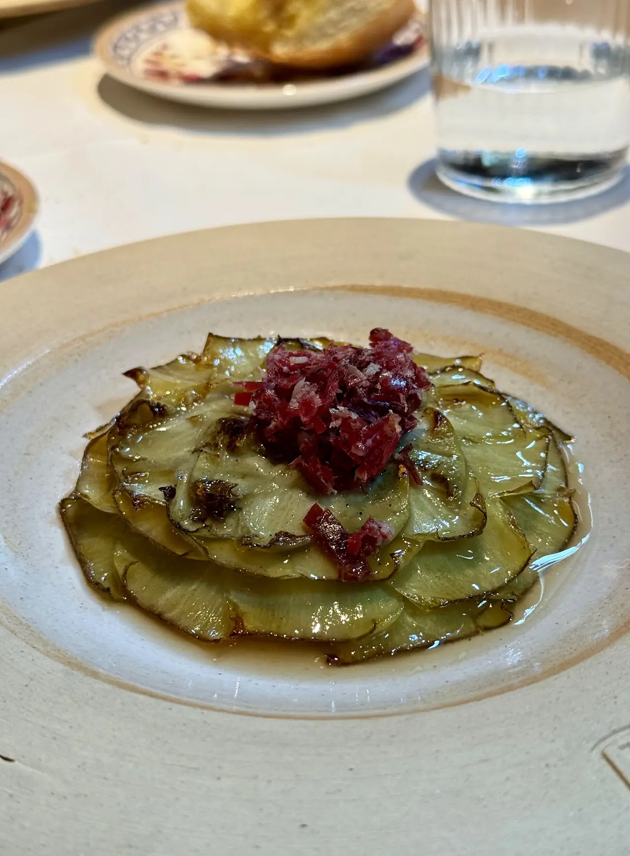 Thinly sliced roasted artichoke topped with a mound of chopped cured ham, drizzled with oil on a stoneware plate