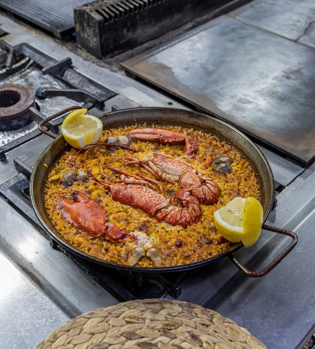 A paella pan with lobster and lemon wedges on a steel stove top