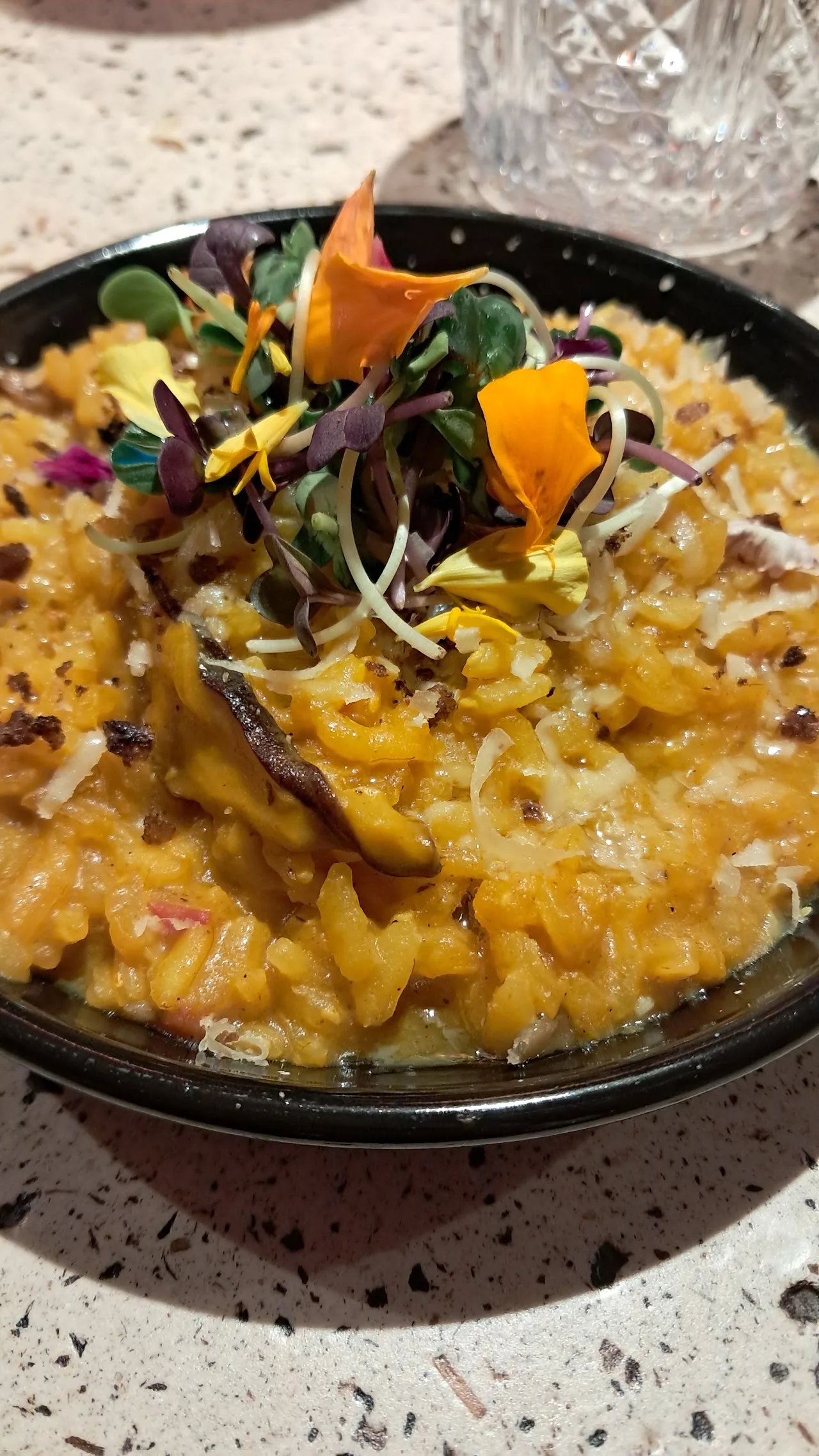 A bowl of risotto garnished with edible flowers and carrot