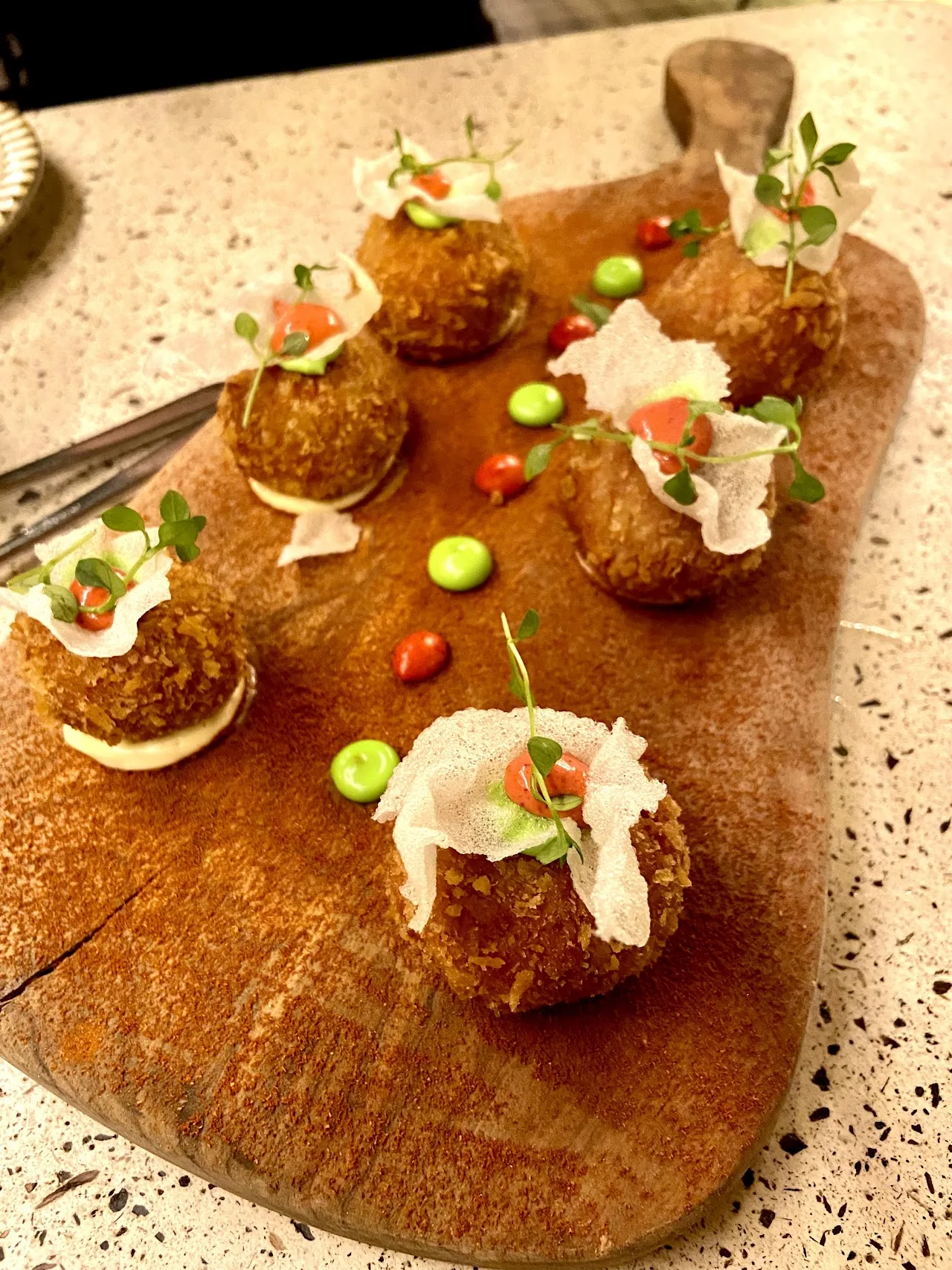 Assorted croquettes on a wooden board with sauce dots