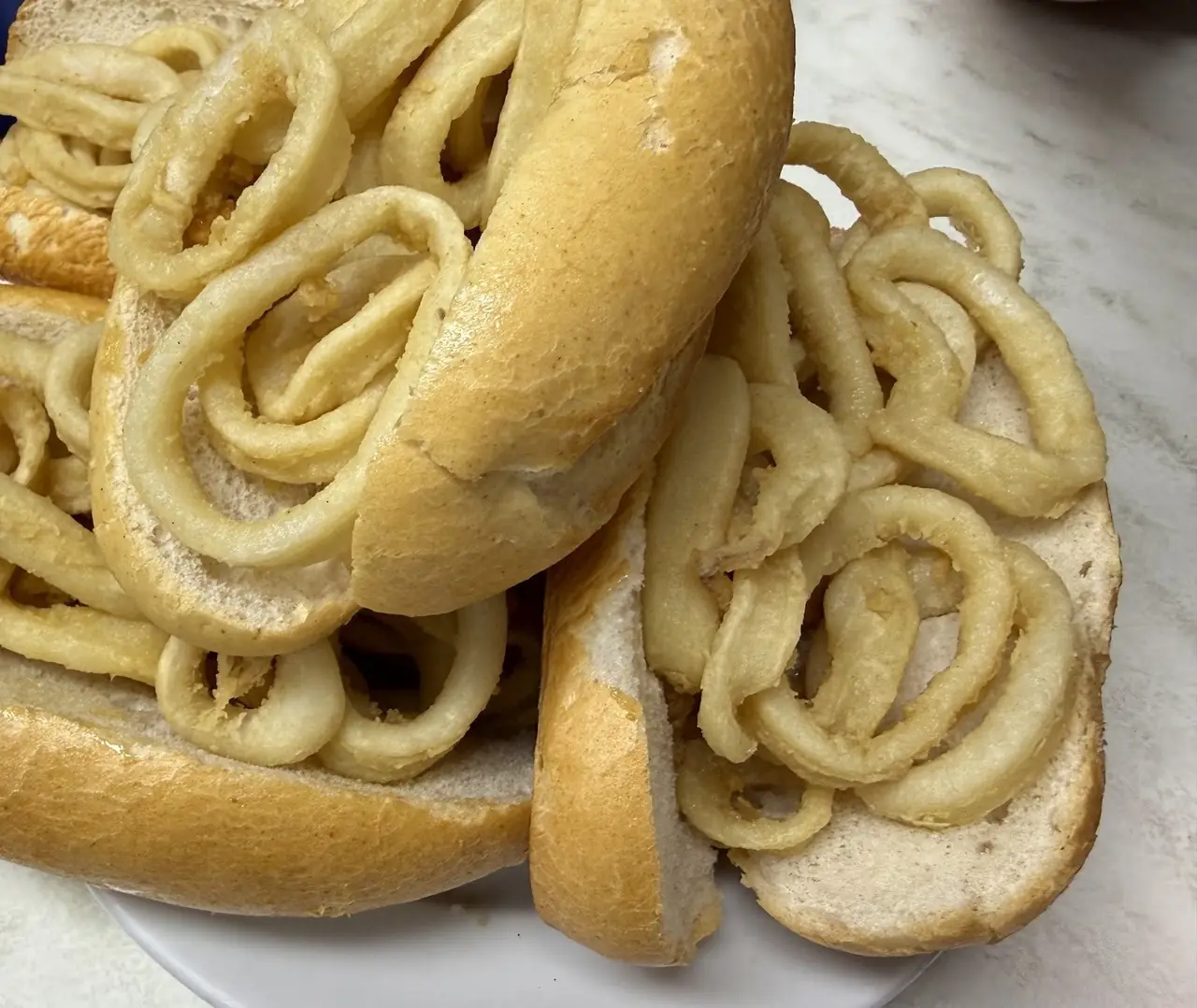 Crusty rolls heaped with fried squid rings on a white plate