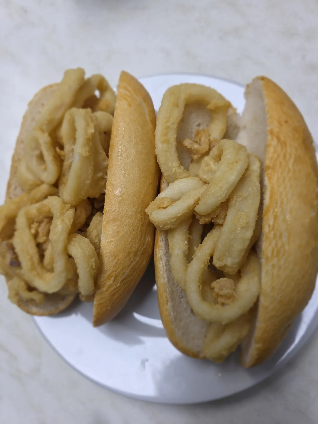 Two halves of a roll packed with fried squid rings on a white plate