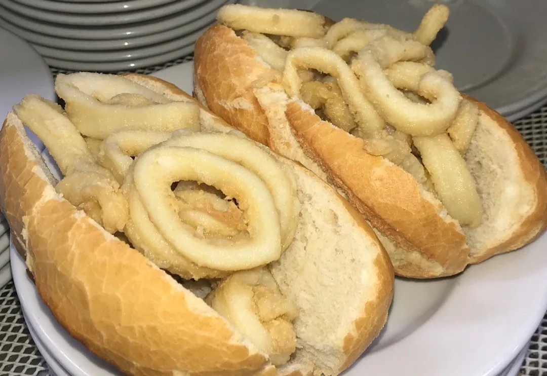 Two crusty rolls filled with fried squid rings on a white plate