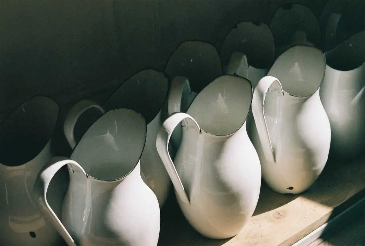 Row of white ceramic pitchers lined up on a wooden shelf, lit by soft side light.