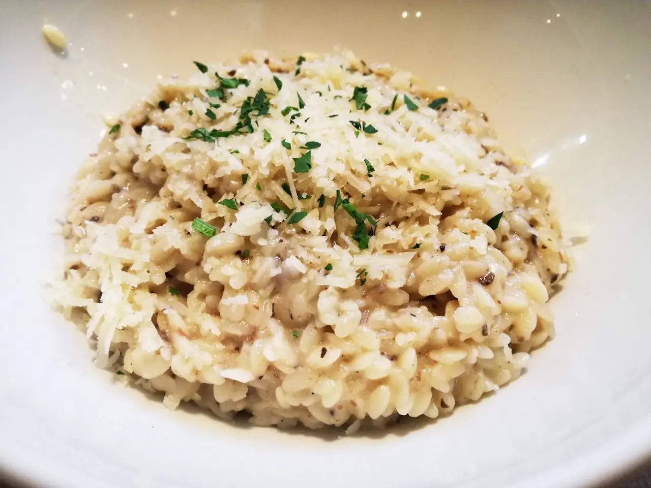 A creamy risotto topped with grated cheese in a white bowl.