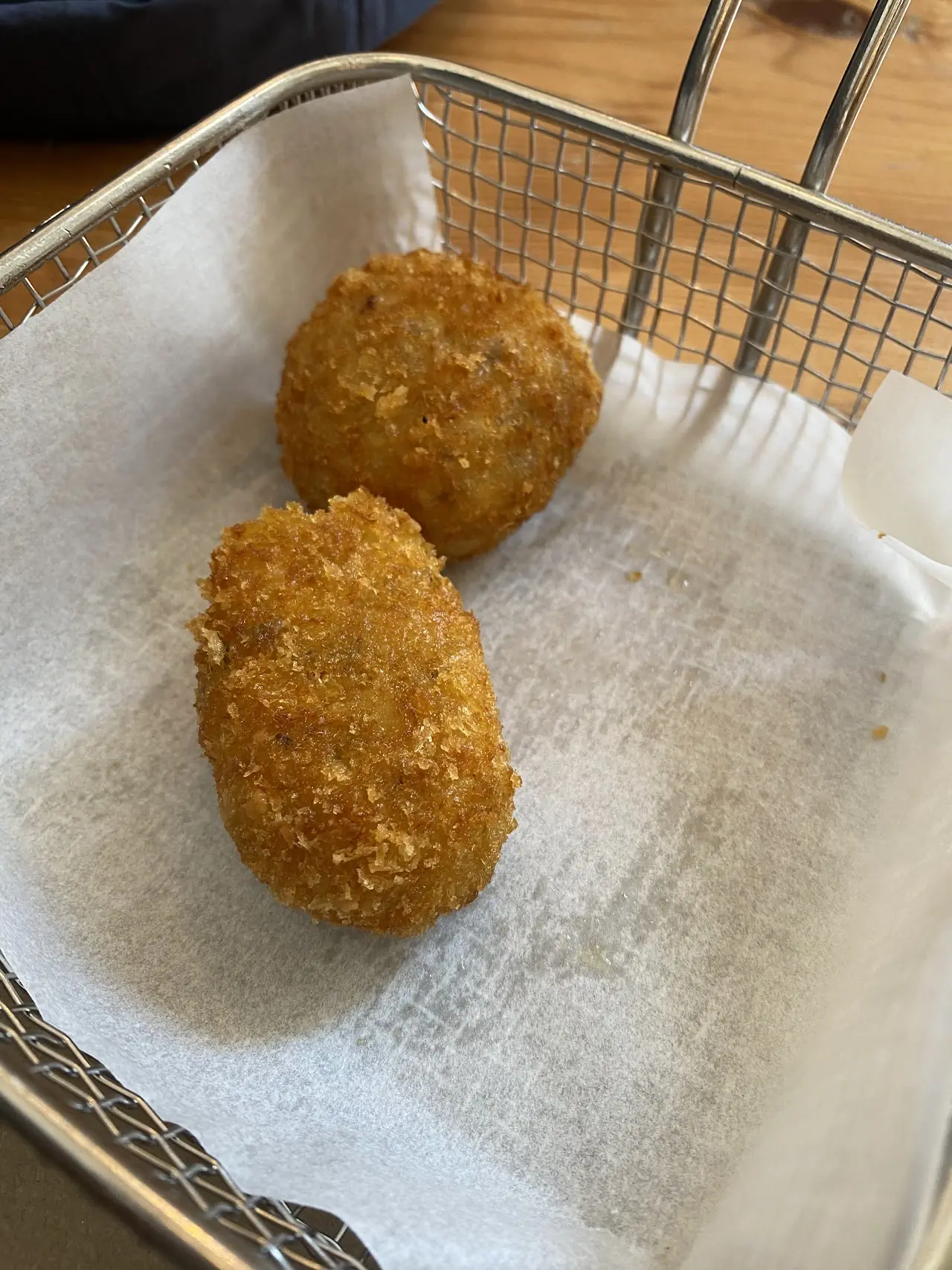 Two golden croquettes in a wire basket lined with paper.