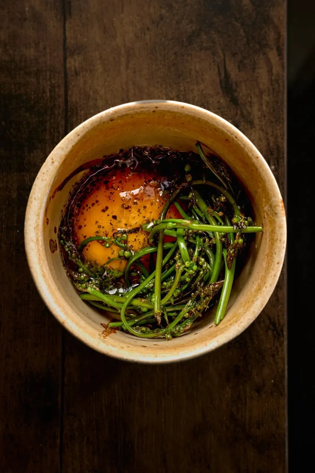 A round bowl with an egg yolk and green vegetables seen from above
