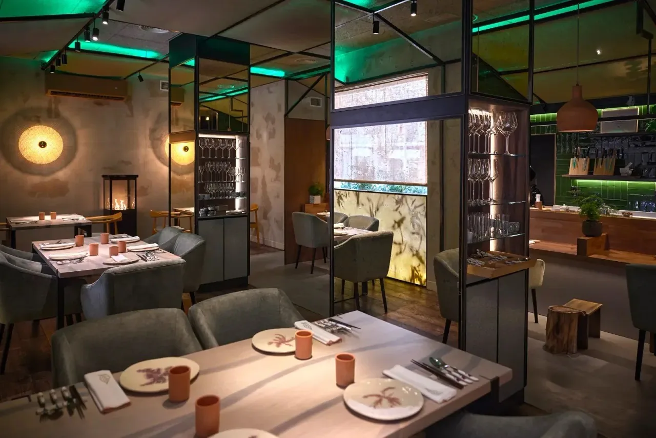 A dining room with set wooden tables, grey chairs, round wall lights and green lighting