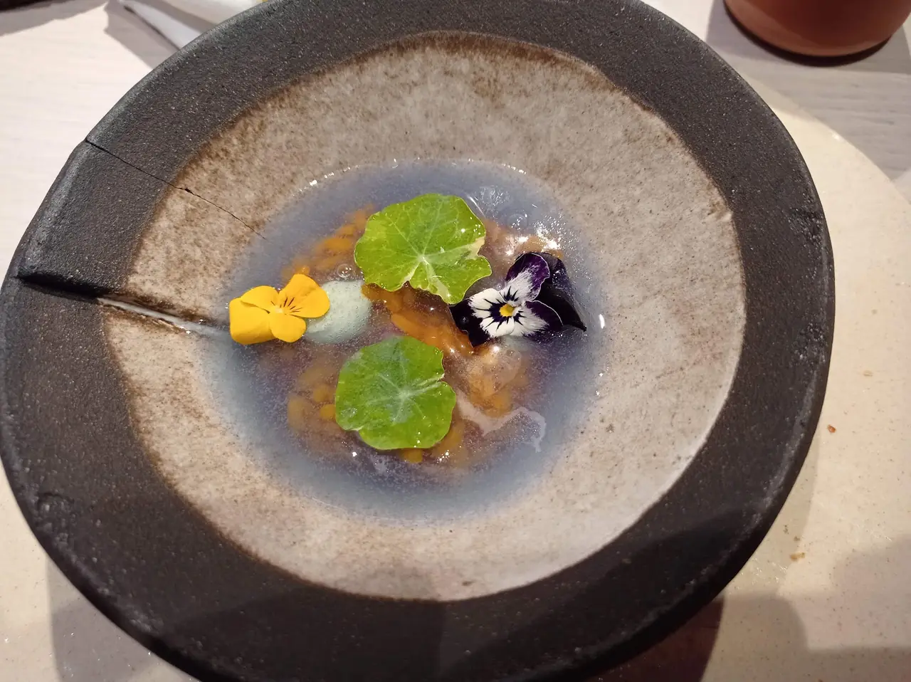 Bowl of clear broth with nasturtium leaves, edible flowers and orange roe-like garnish