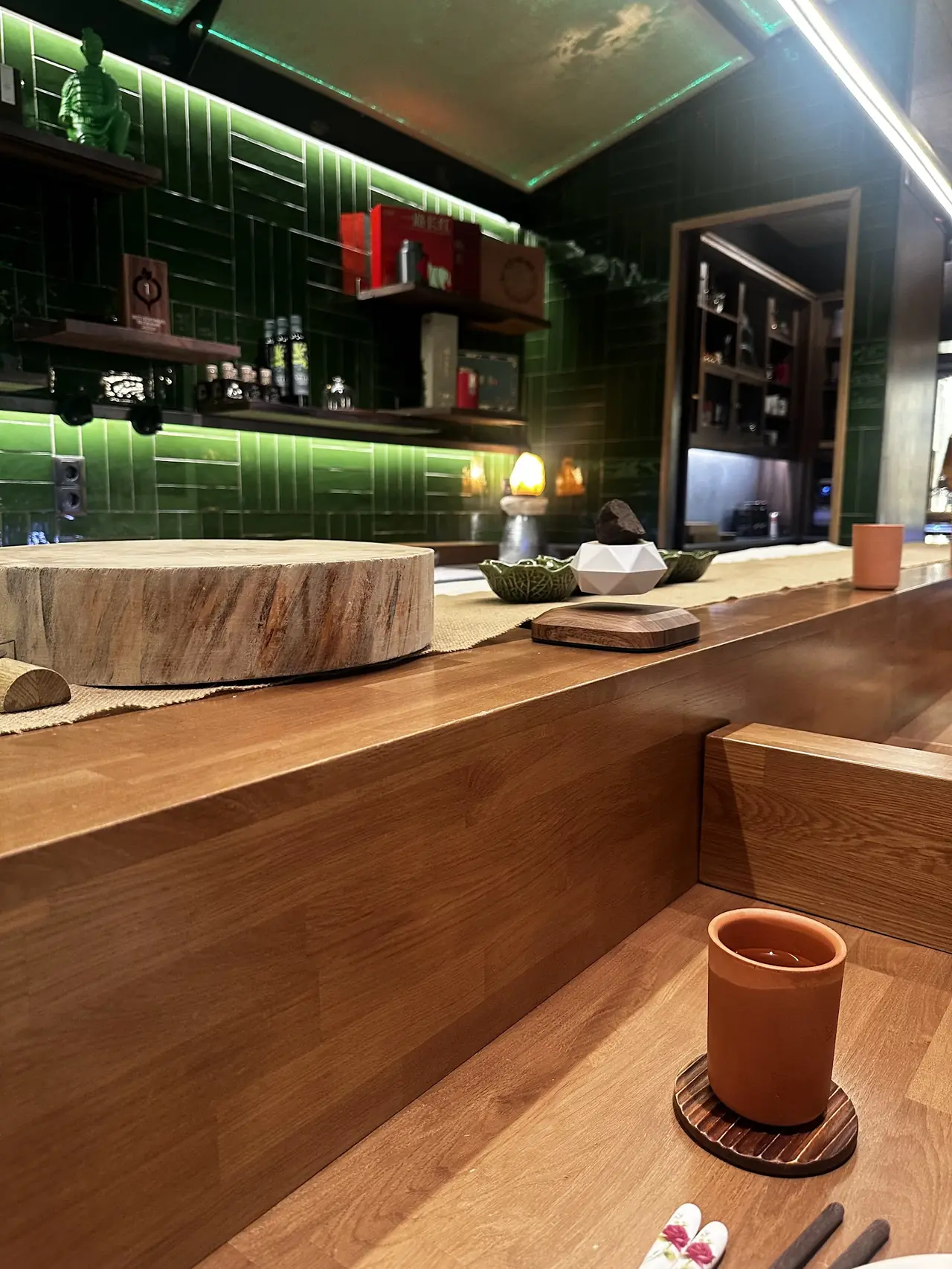A terracotta cup filled with dark tea on a wooden coaster at a green-tiled bar counter