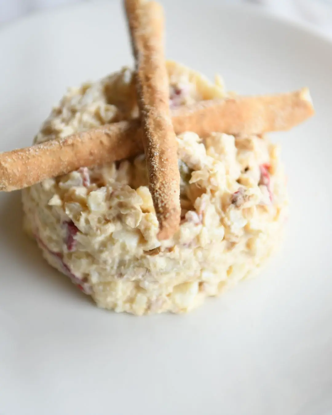 Close-up of a seafood salad topped with crossed breadsticks on a white plate