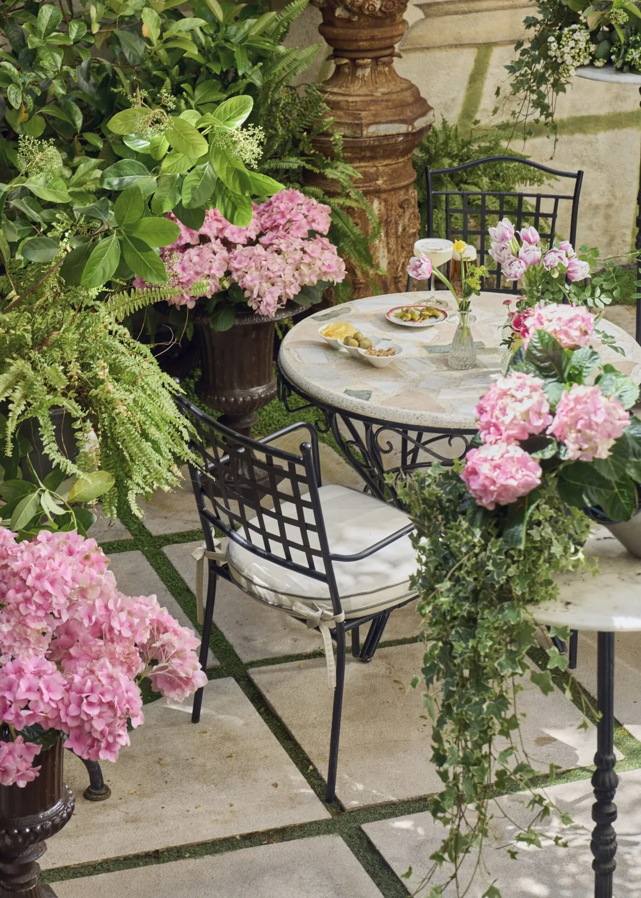 A small round terrace table with pink hydrangeas and ferns on a patterned tiled floor