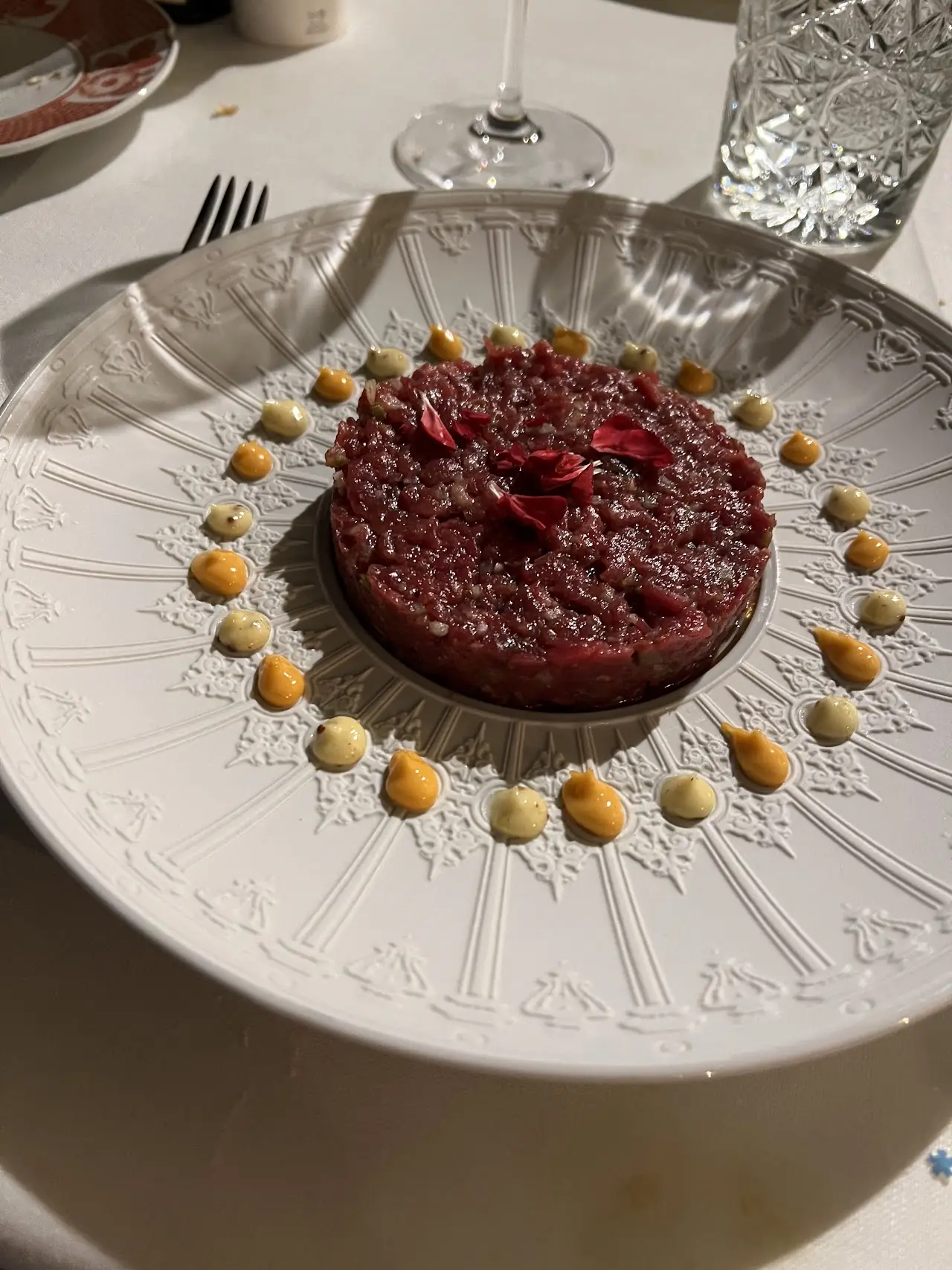 Dark red disc-shaped dish on an ornate silver plate, encircled by small golden dots of sauce.