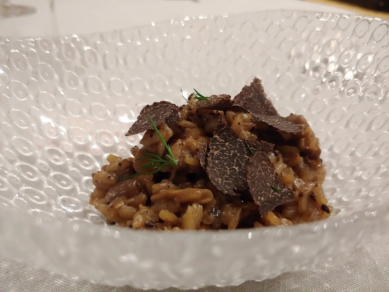 Rice dish topped with shaved black truffle, served in a textured glass bowl.