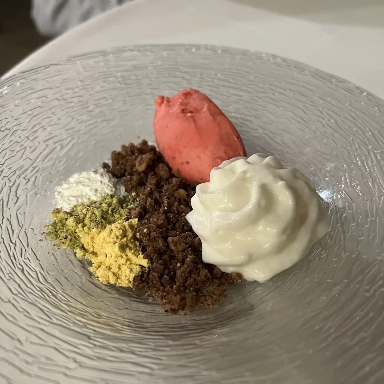 Dessert plate with a pink sorbet scoop, whipped cream, and a dark crumble.