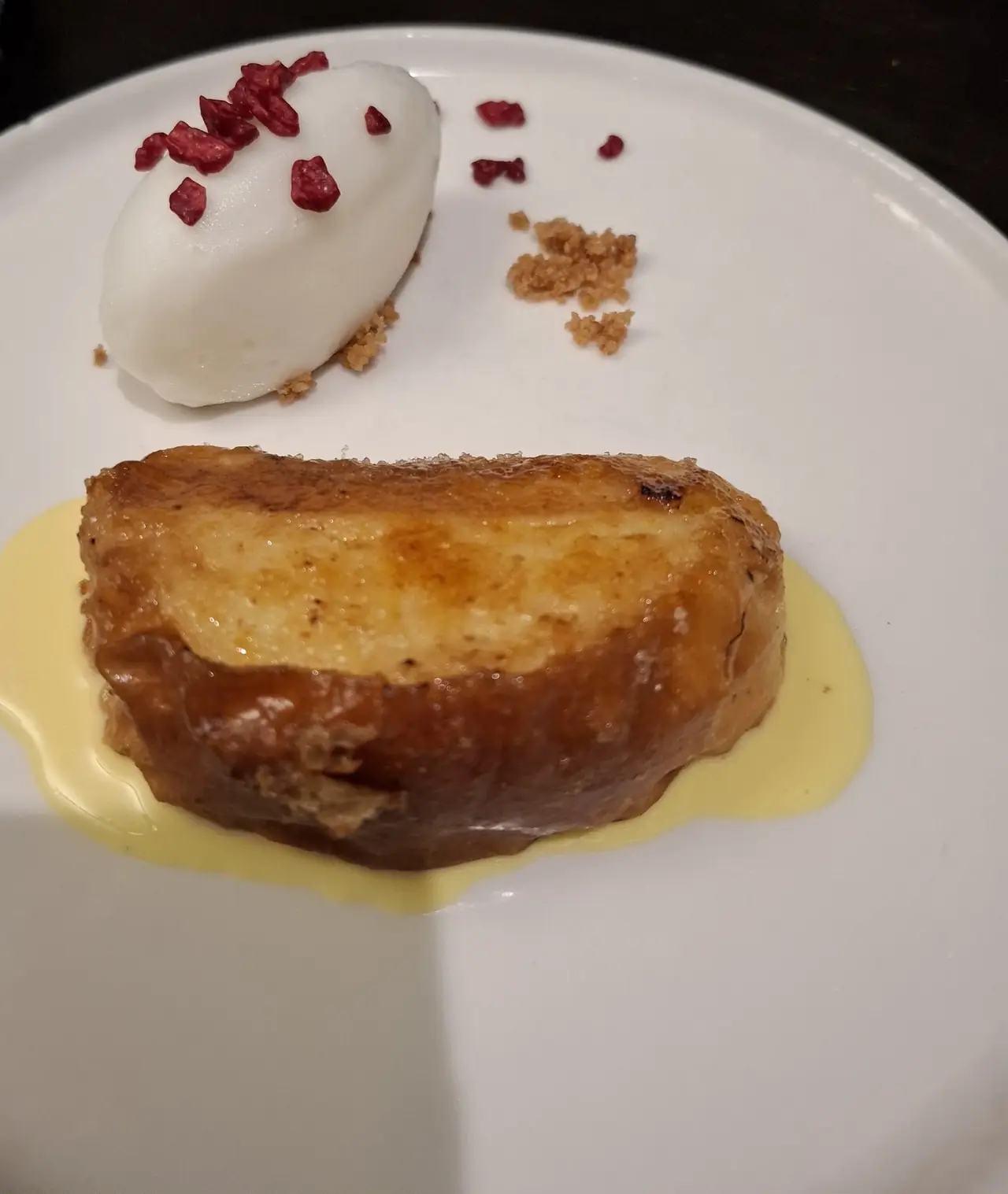 A caramelised torrija in a pool of custard, with a quenelle of ice cream topped with freeze-dried raspberries