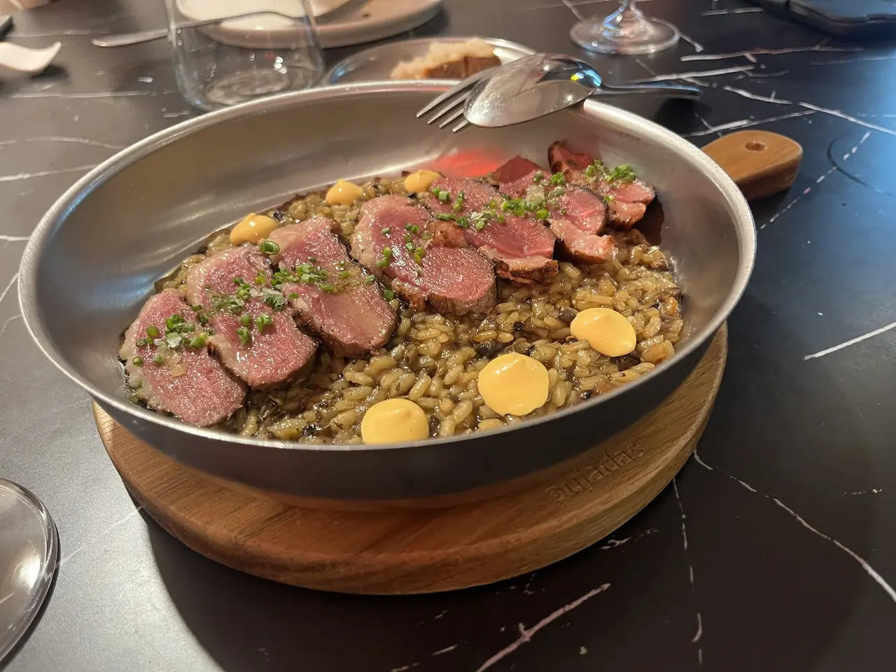 Sliced pink meat over rice in a metal pan with sauce dots