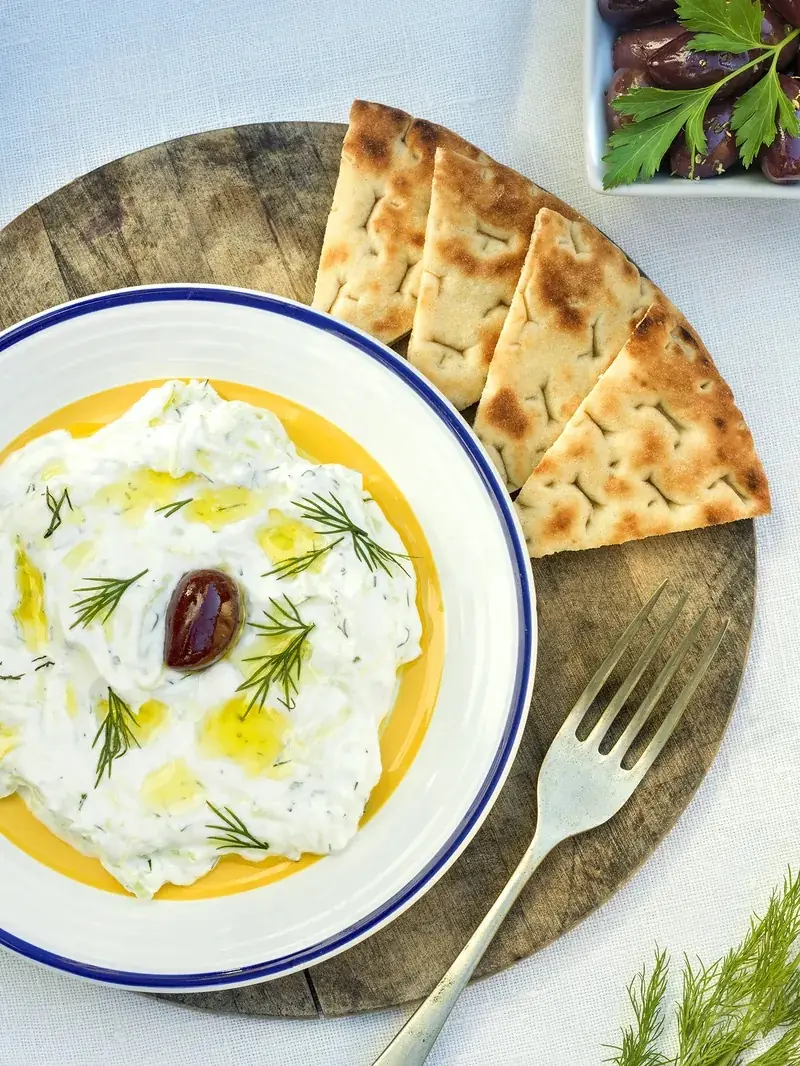 Tzatziki with olive oil, a whole olive, and dill, served with grilled pita triangles and a side of olives, at El Magraner Boig