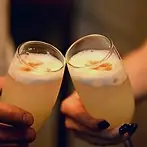 Two pisco sour cocktails with frothy tops being clinked together in a toast