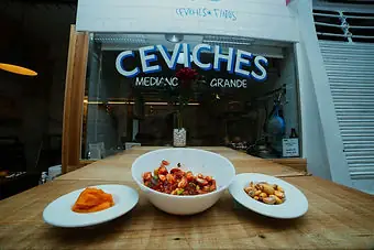 Ceviche bowl and two side dishes on a table in front of the venue's lit ceviches counter signage