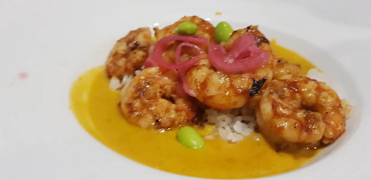 Grilled shrimp served over rice with a citrus sauce and pickled onion