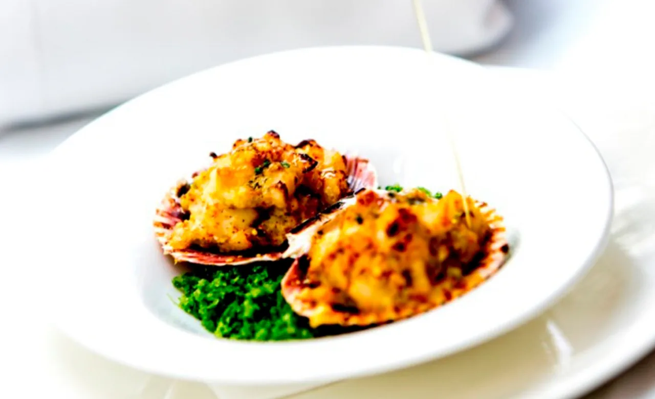 Two baked shells with a golden topping on a green purée in a white bowl