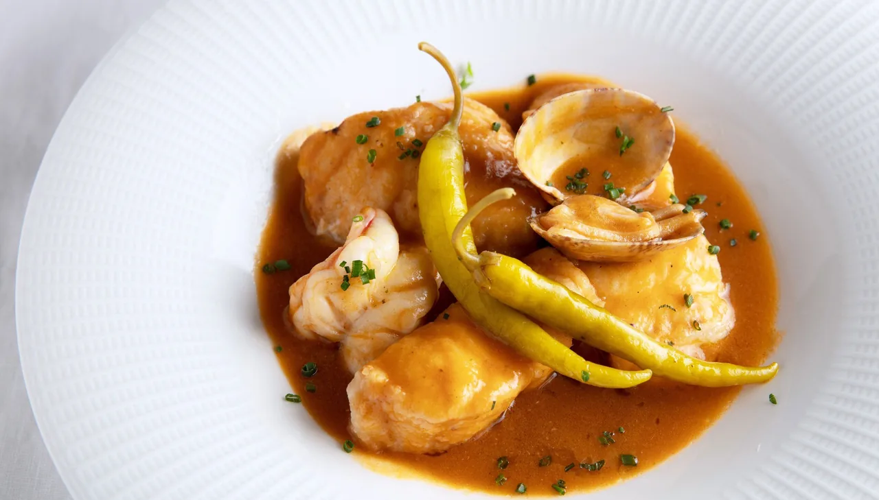 Pieces of seafood with a green pepper in an orange sauce on a white plate