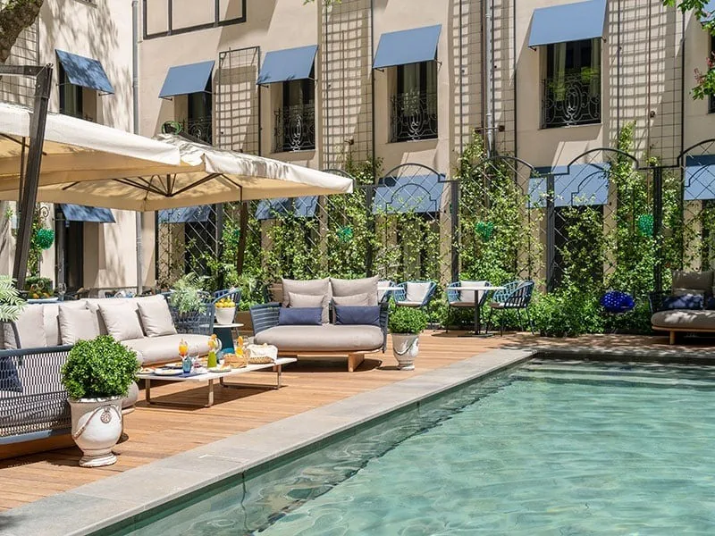 A courtyard terrace with cushioned seating and parasols beside a long swimming pool