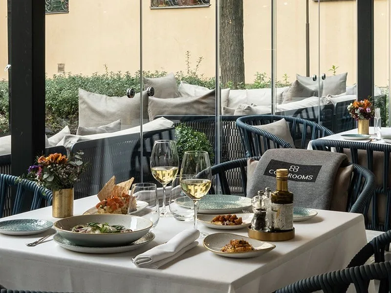 A glass-enclosed terrace with a table set with several dishes and wine glasses