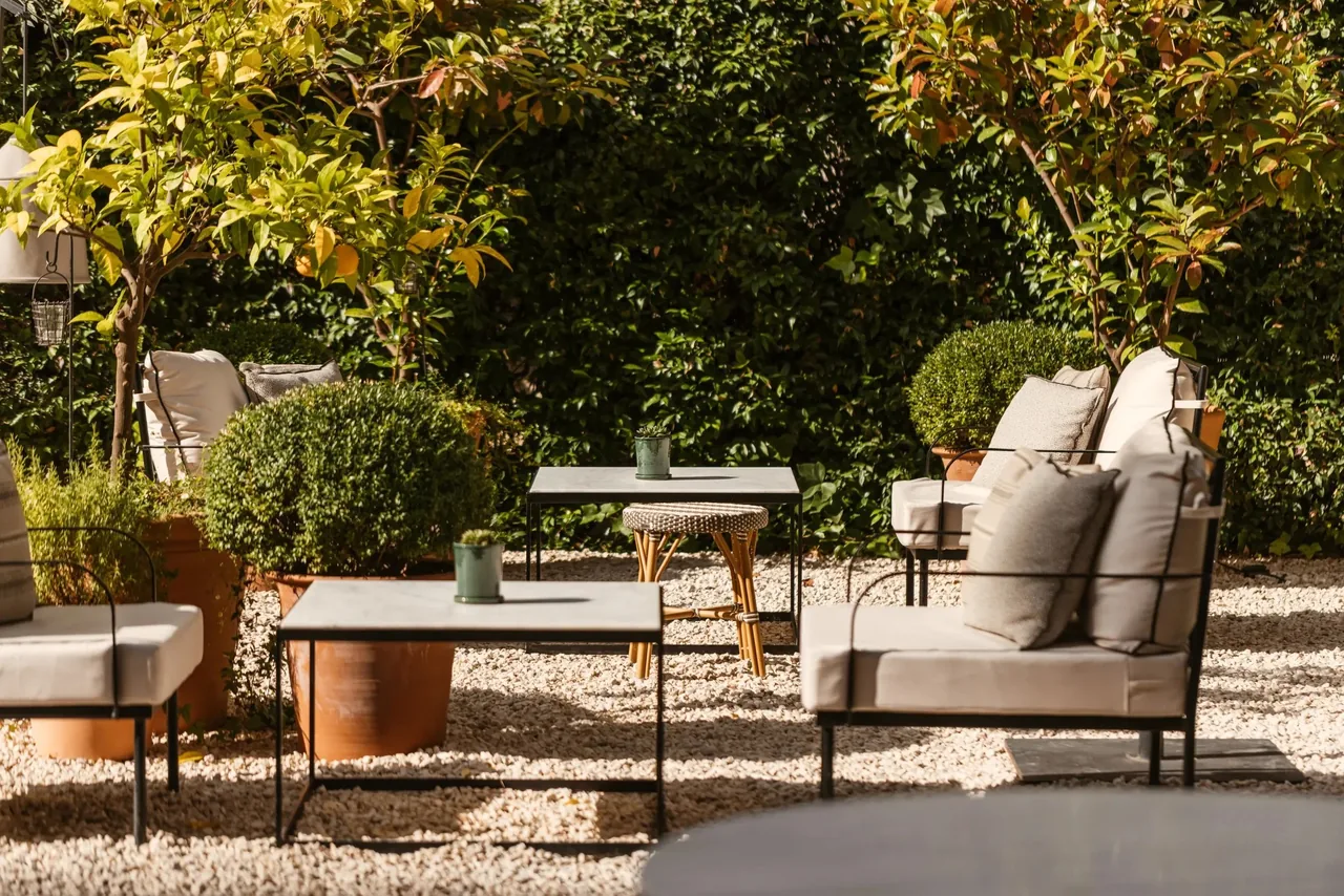 A garden terrace with cushioned seating and low tables among trimmed shrubs