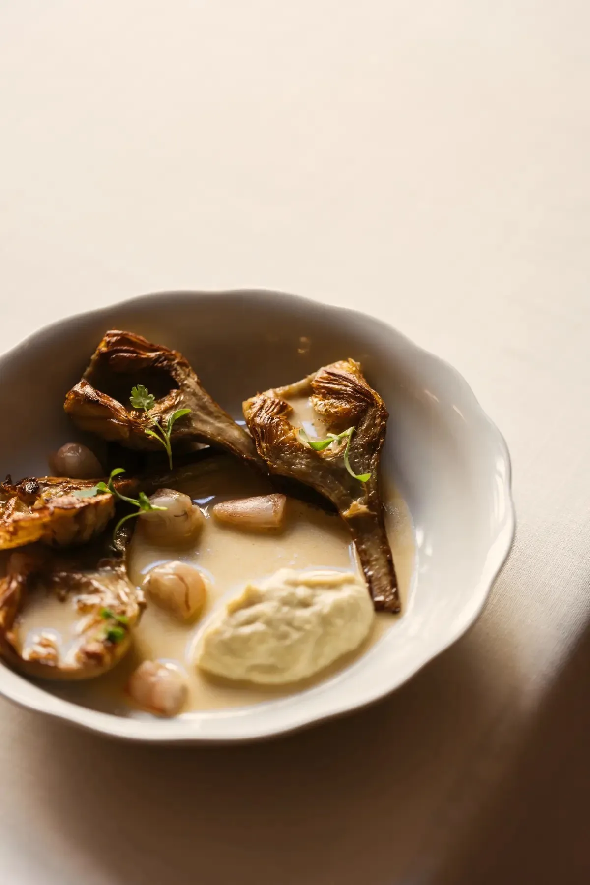 A white bowl of artichokes with a creamy puree on a white table