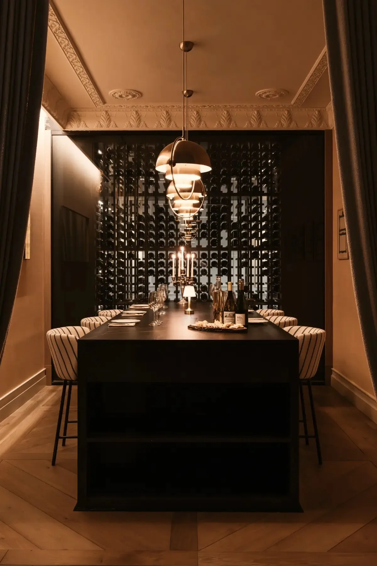 A dark private dining room with a long table and a glass wine wall behind it