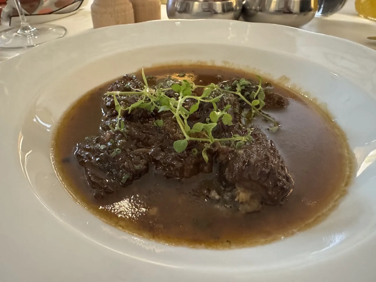 A braised meat dish in a rich brown sauce, topped with microgreens