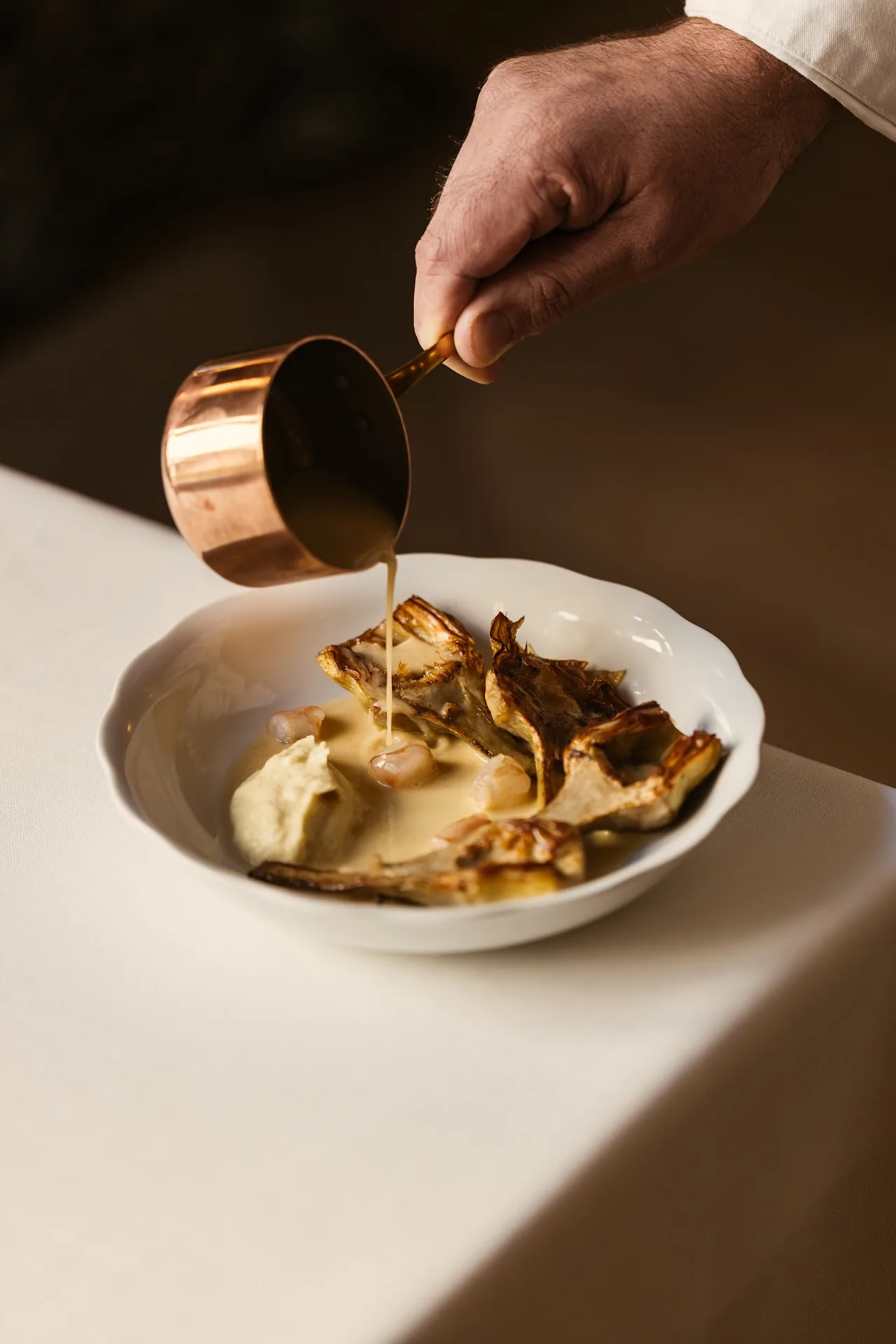 A chef pouring golden sauce over a mushroom dish
