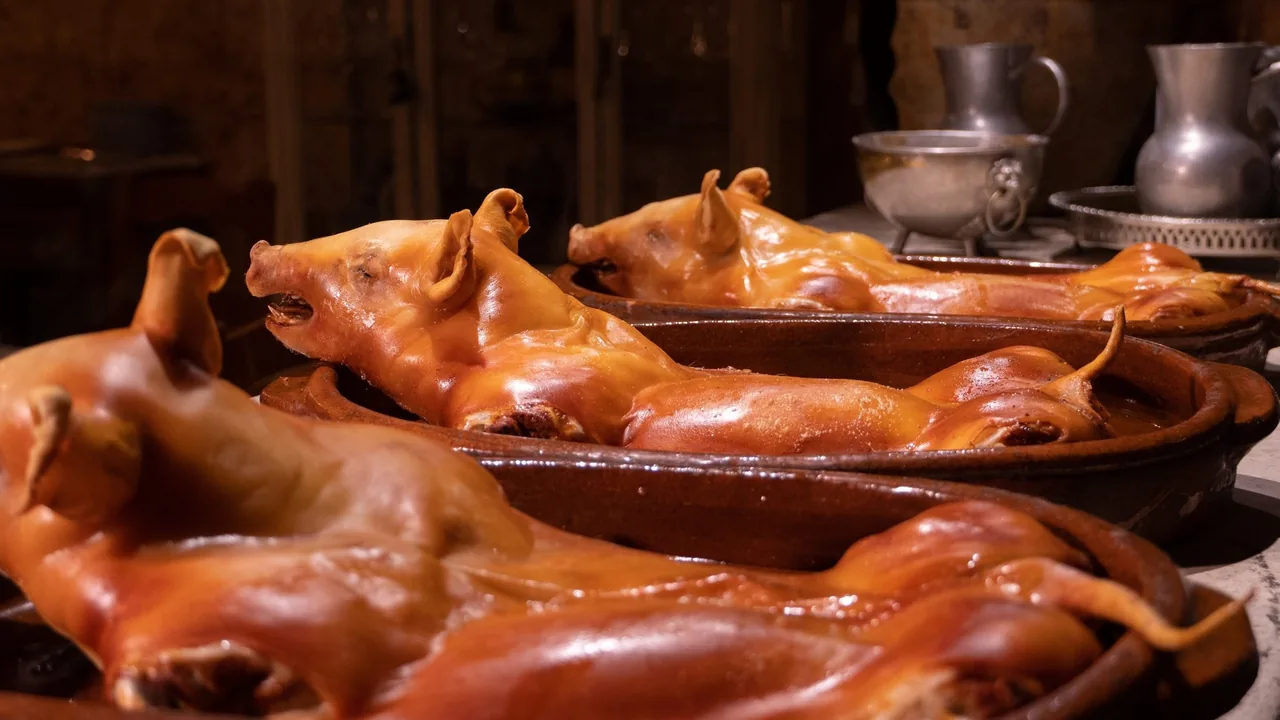 Three whole roast suckling pigs lying in clay dishes with pewter jugs behind them