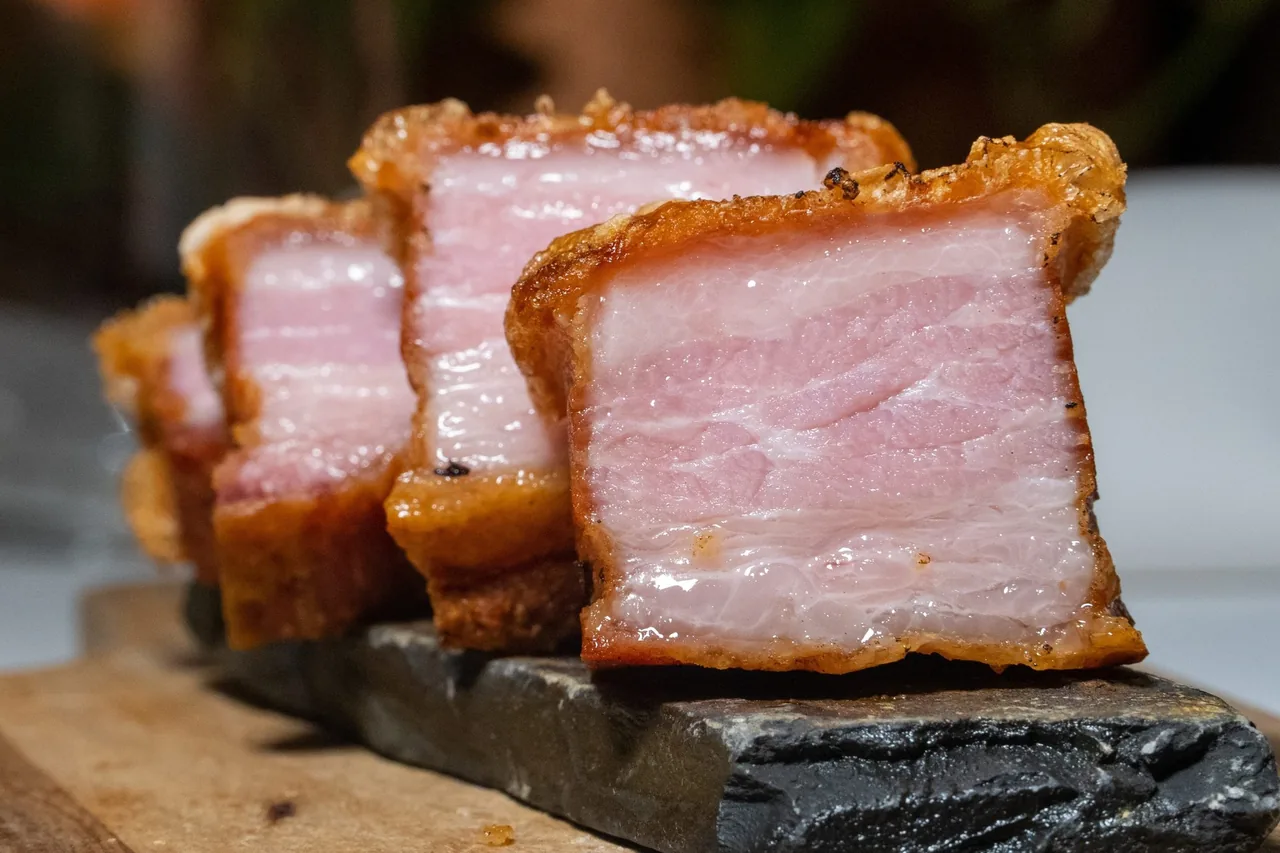 Thick cut pieces of roast suckling pig with golden crackling skin on a slate board