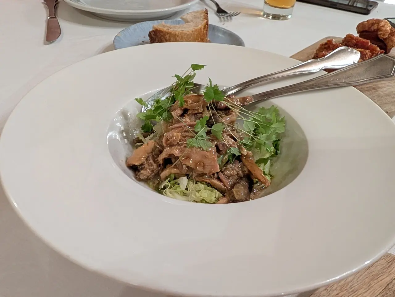 Shredded braised meat over lettuce topped with parsley in a wide white bowl