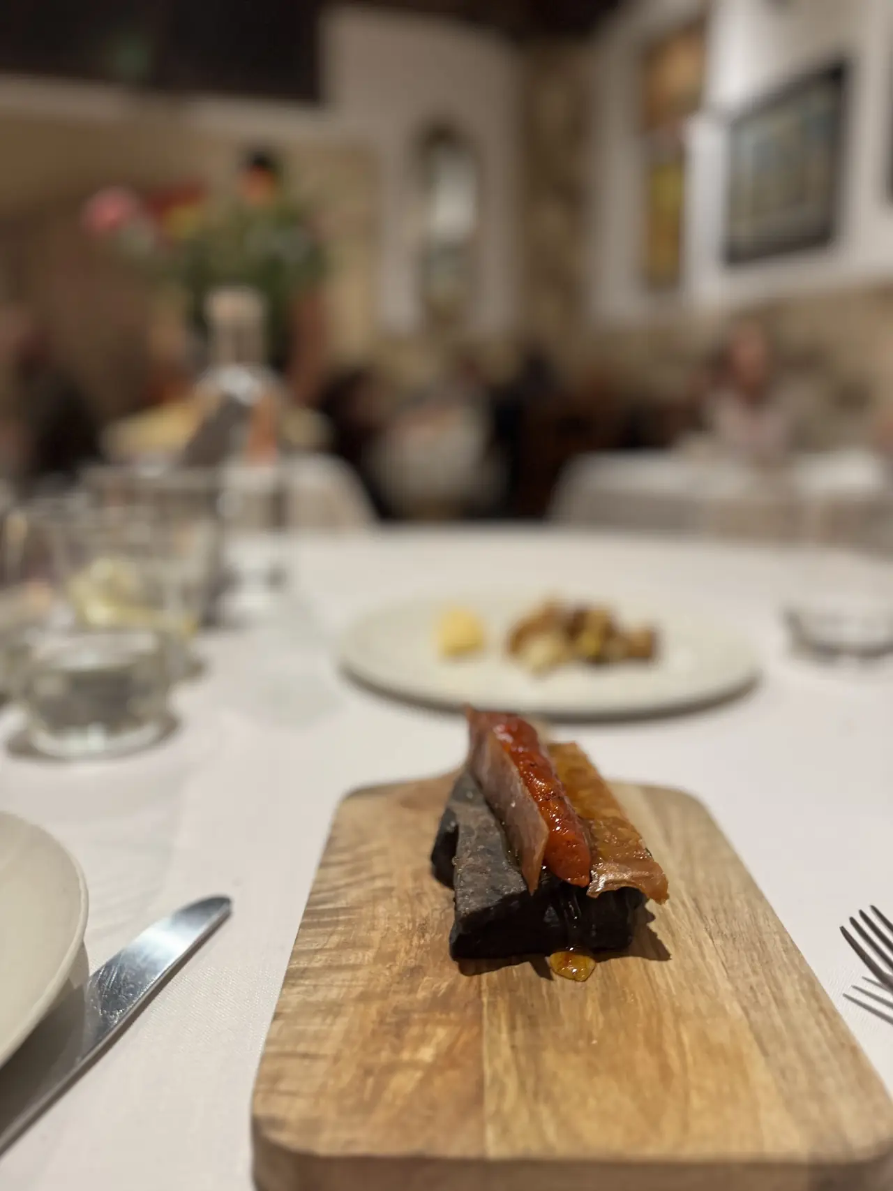 A slice of black pudding and cured meat with a red sauce served on a small wooden board