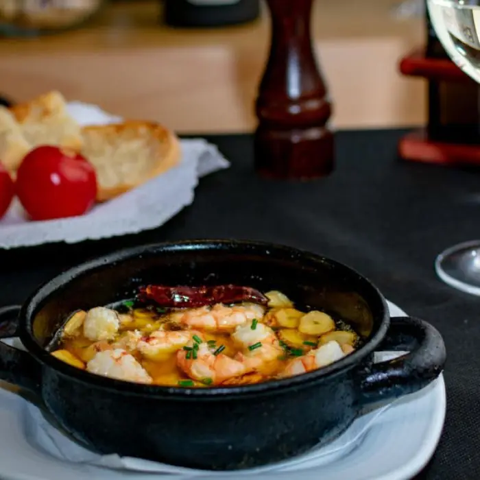 Cazuela of sizzling prawns and garlic in olive oil with a dried chili pepper, served with bread and tomatoes on the side, at El Pescadito de Mandri