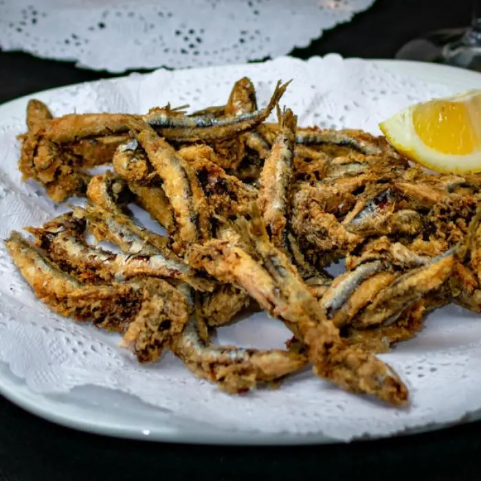 Plate of fried small whole fish (pescaditos fritos) with a lemon wedge on a paper doily, at El Pescadito de Mandri