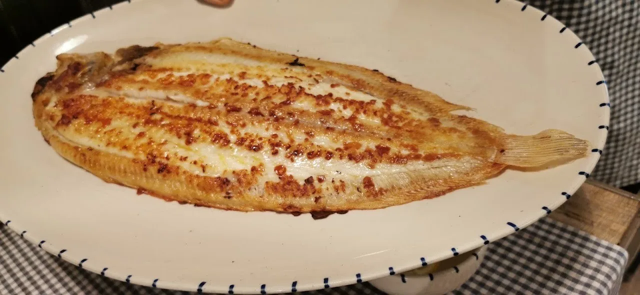 A whole grilled flatfish on a white oval plate with a blue rim