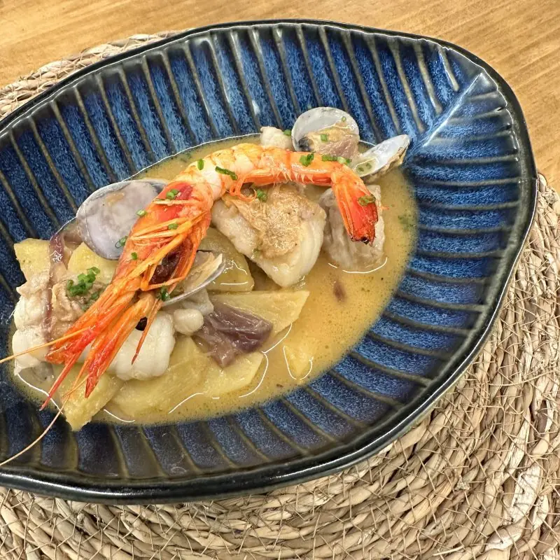 Seafood stew with prawn, clams, monkfish, and potatoes in a dark ceramic bowl at El Provisional
