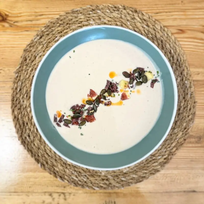 Creamy soup with toasted pumpkin seeds and dried fruit garnish in a teal-rimmed bowl at El Provisional